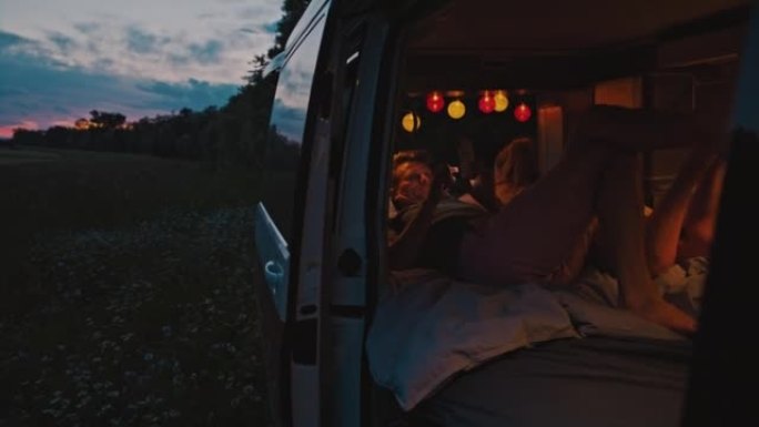 WS夫妇躺在黄昏时停在草地上的露营车内