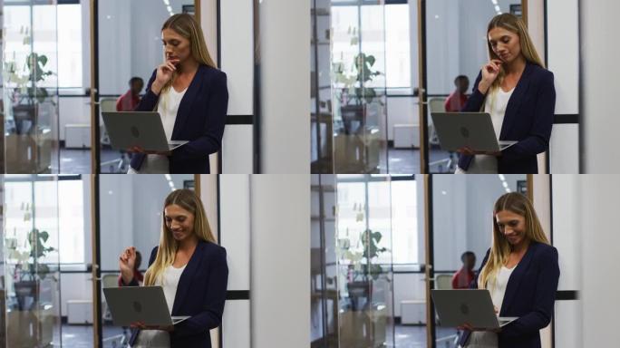 微笑的白人妇女站在现代办公室时使用笔记本电脑