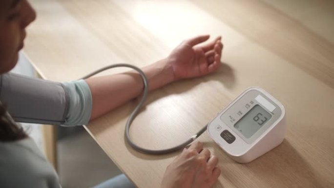 使用监视器的亚洲妇女在家中测量自己的血压