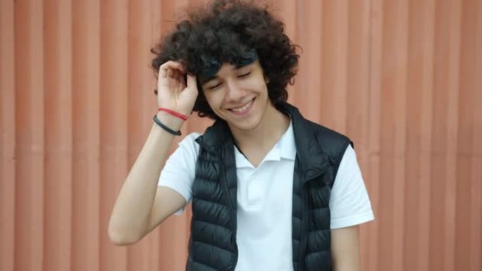 时尚的中东少年少年举着太阳镜在户外微笑的慢动作肖像