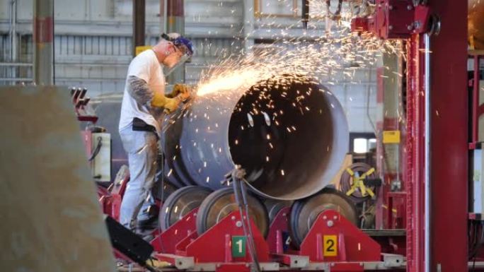 金属工人在工厂的大圆筒上使用研磨机