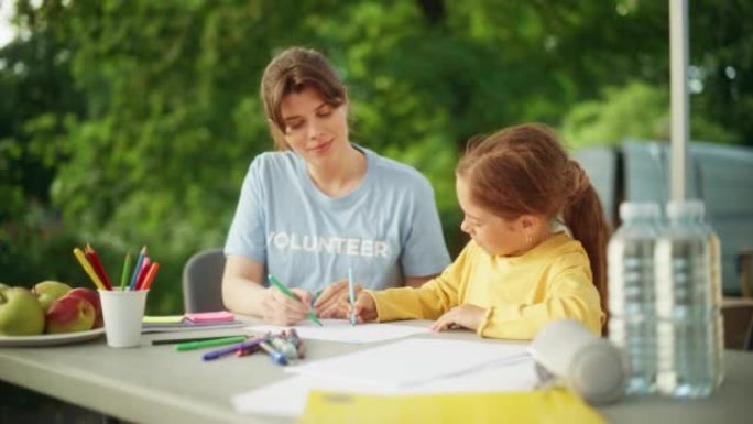 当地人道主义援助组织的志愿者教一个才华横溢的小女孩用五颜六色的蜡笔画画。快乐的孩子和慈善工作者在幼儿