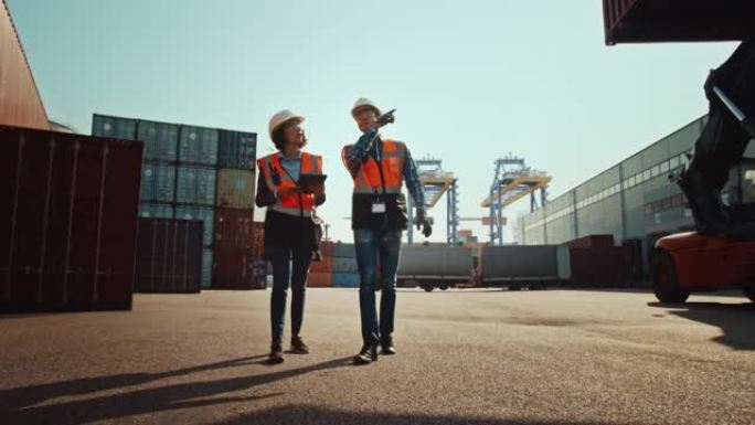 带平板电脑的多种族女工业工程师和戴着安全帽和安全背心的男工头工人在集装箱码头行走。VFX双梁龙门起重