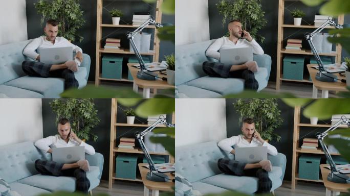 有魅力的家伙在手机上讲话并使用笔记本电脑在家工作的肖像