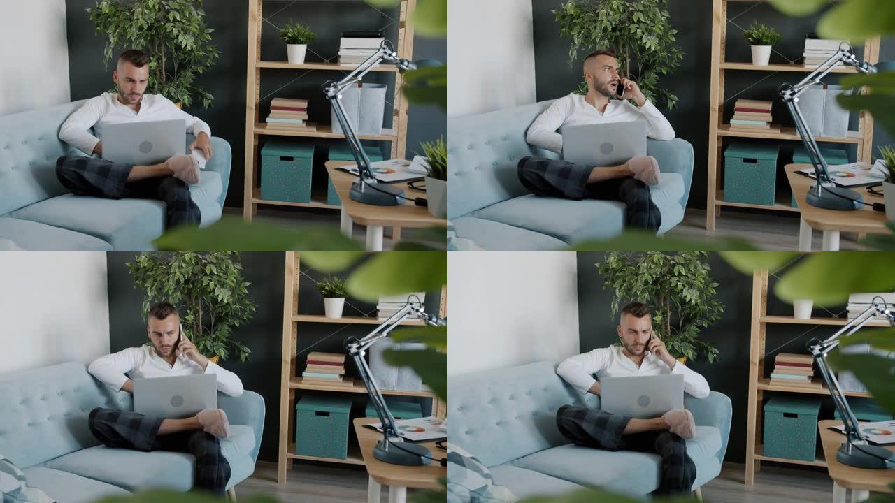 有魅力的家伙在手机上讲话并使用笔记本电脑在家工作的肖像