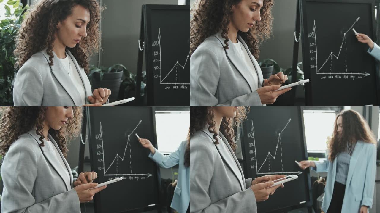女商人在同事做演讲时使用平板电脑