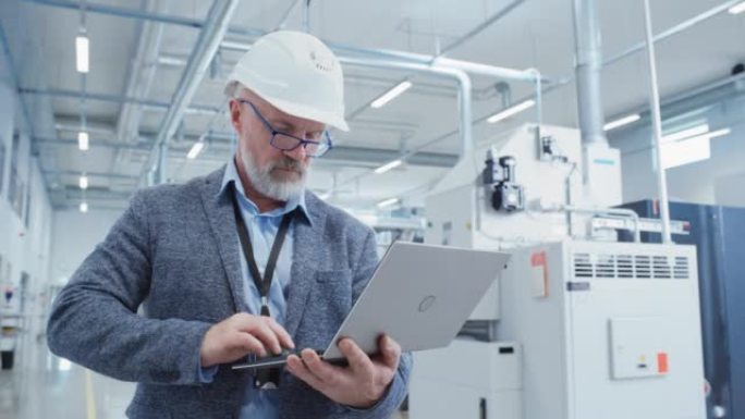 一位留着胡子的中年总经理站在工厂里，穿着便服，戴着白色安全帽的肖像。从事笔记本电脑工作的重工业专家。