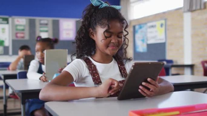 快乐的混血女学生坐在教室里，使用平板电脑，看着相机的肖像