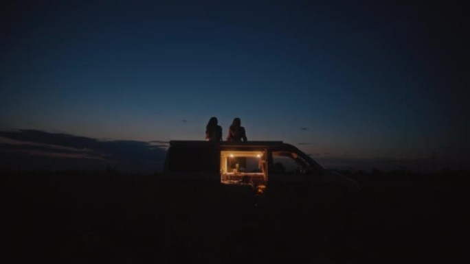 DS两名妇女晚上在田野中央的露营者屋顶上放松