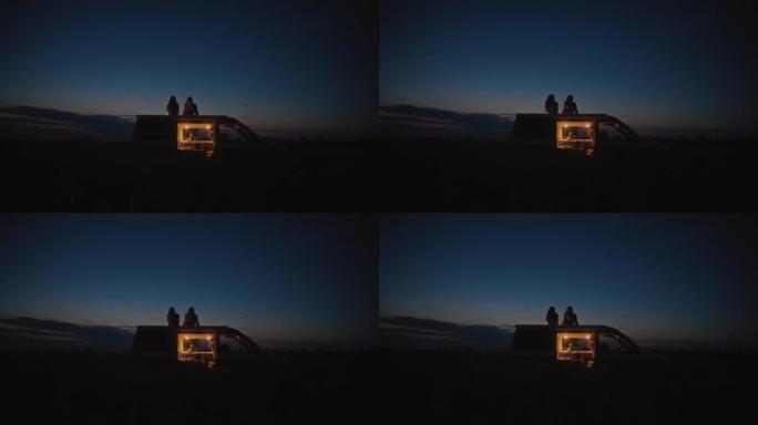 DS两名妇女晚上在田野中央的露营者屋顶上放松