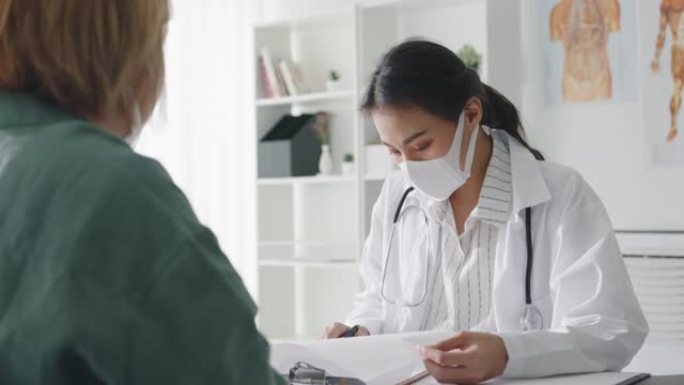 年轻的亚洲女士医生戴防护口罩使用剪贴板正在与医院的女孩患者讨论结果或症状发表重大新闻谈话。