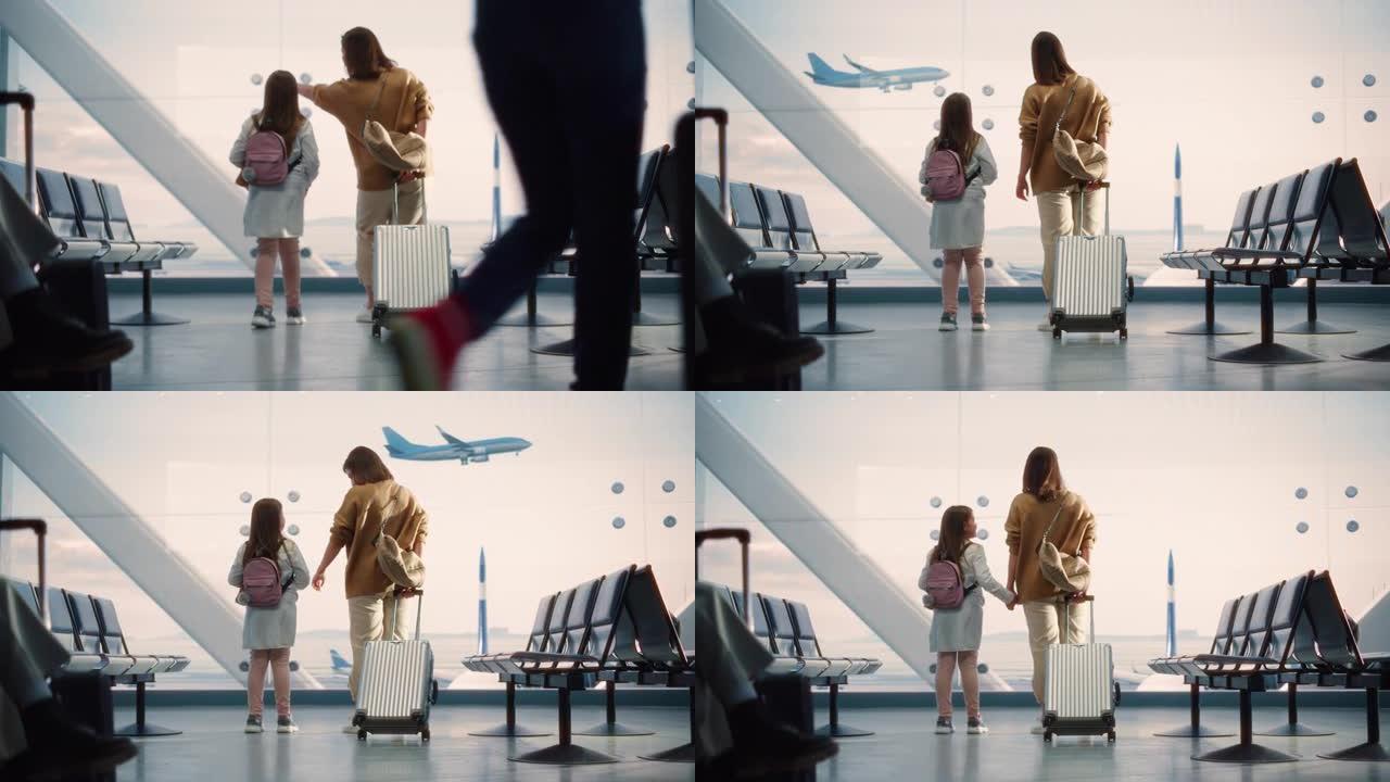 机场航站楼: 美丽的母亲和可爱的小女儿等待他们的假期航班，看着窗外的飞机进出。航空枢纽登机休息室的年
