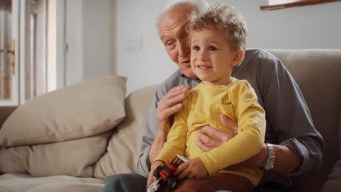 孩子和祖父之间的美好时光: 老人看电视并与孙子交谈。这个可爱的小男孩正在与他的祖父分享和解释他最喜欢