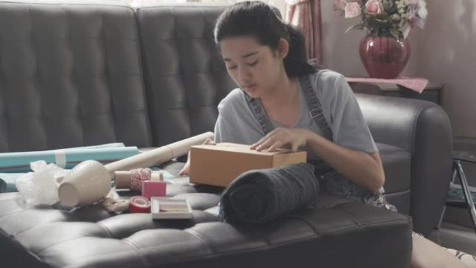 潘右铜: 亚洲年轻少女制作手工物品护理包。可爱的女孩打包一个包装箱，准备从远处寄给她的家人或朋友。