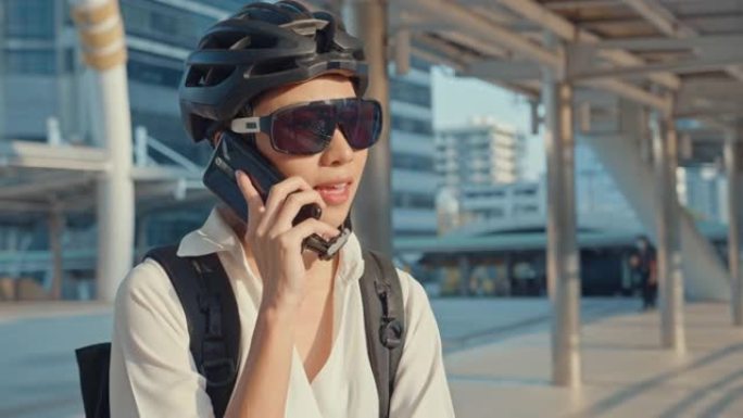 带背包的亚洲女商人打电话给手机，电话在城市街道上微笑着去办公室上班。体育女孩用手机做生意。