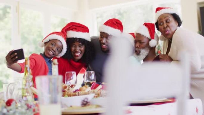 戴着圣诞老人帽子的非裔美国人家庭坐在餐桌上在智能手机上自拍哈