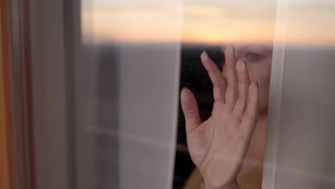 斯洛·莫忧郁的女人在回家命令期间透过窗户看时，把手放在窗户上