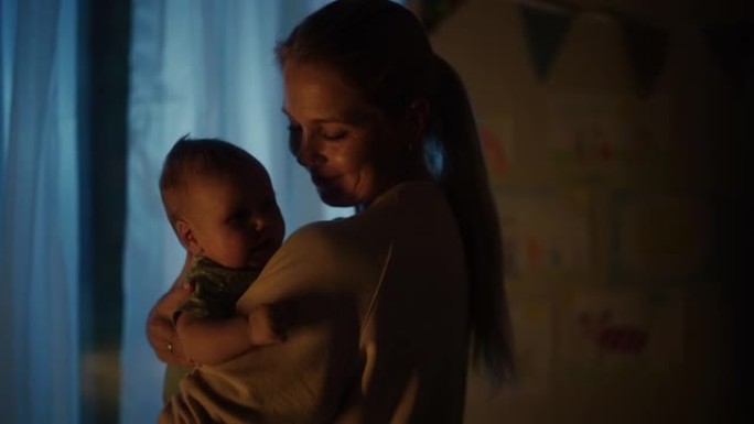 快乐的母亲晚上在舒适的黑暗儿童卧室里抱着一个可爱的新生婴儿。有爱心的妈妈和幼儿在家里结为纽带。童年、