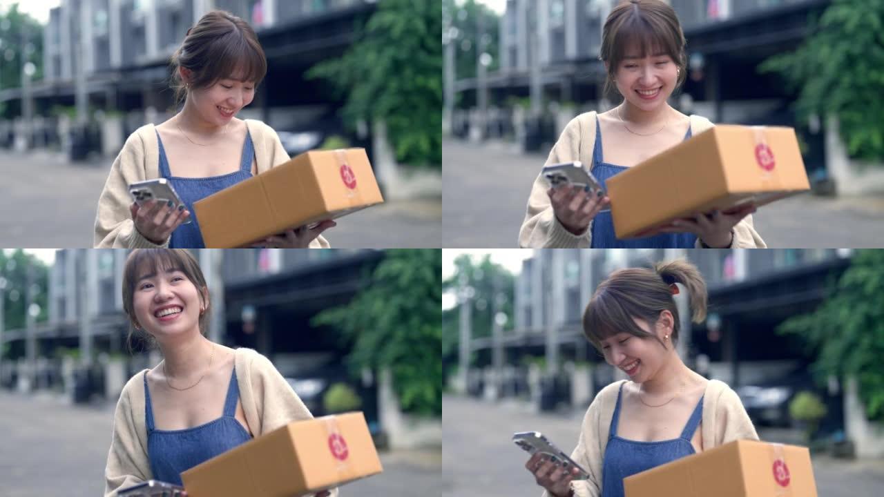 年轻的亚洲妇女在家中携带一堆送货箱时在手机上阅读信息