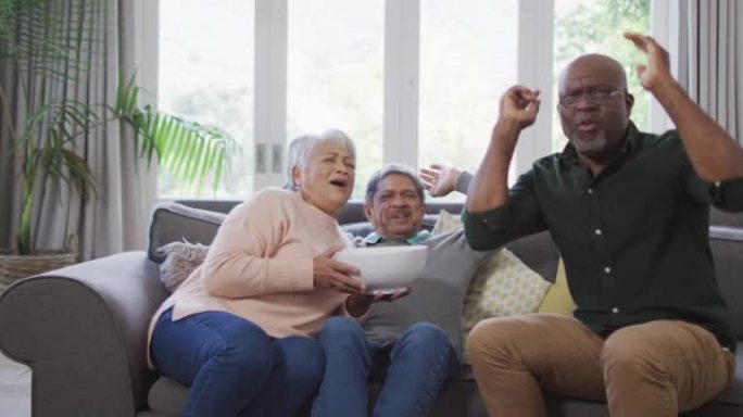 快乐的混血儿高级夫妇和非裔美国朋友用爆米花看电视