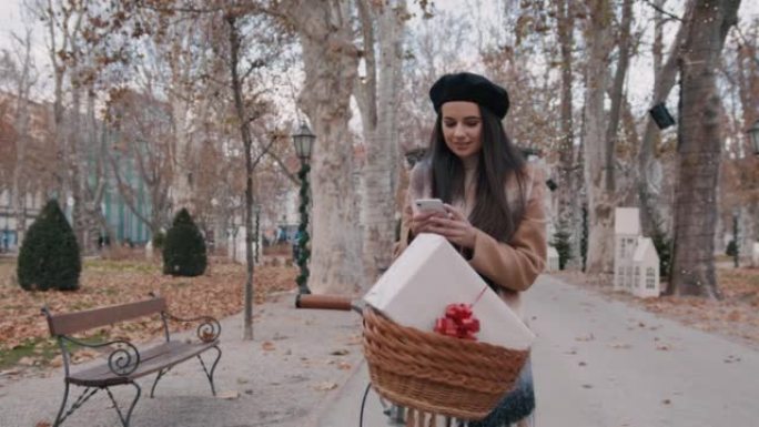 年轻女子在自行车上使用带礼物的手机