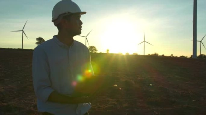 在风力发电站工作的年轻男工程师的剪影日落，检查风车农场的能源生产。可再生能源工厂概念。