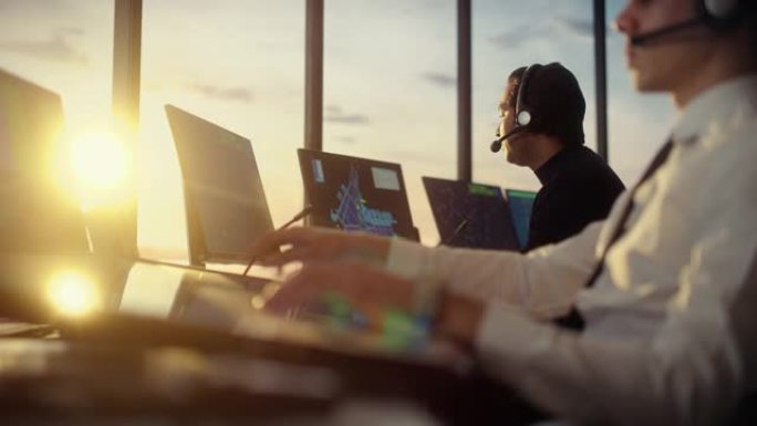 戴着耳机的男性空中交通管制员在机场塔楼通话。办公室充满了台式计算机显示屏，带有导航屏幕，飞机出发和到