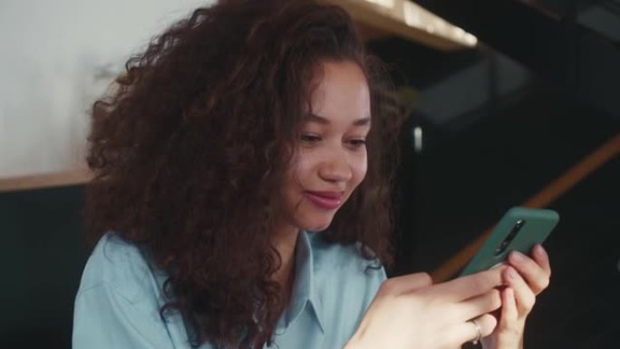 使用智能手机购物应用程序，特写美丽快乐的年轻非洲裔美国学生女子与惊人的卷发。
