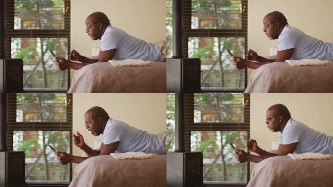 快乐的非洲裔美国老人躺在床上看平板电脑欢呼