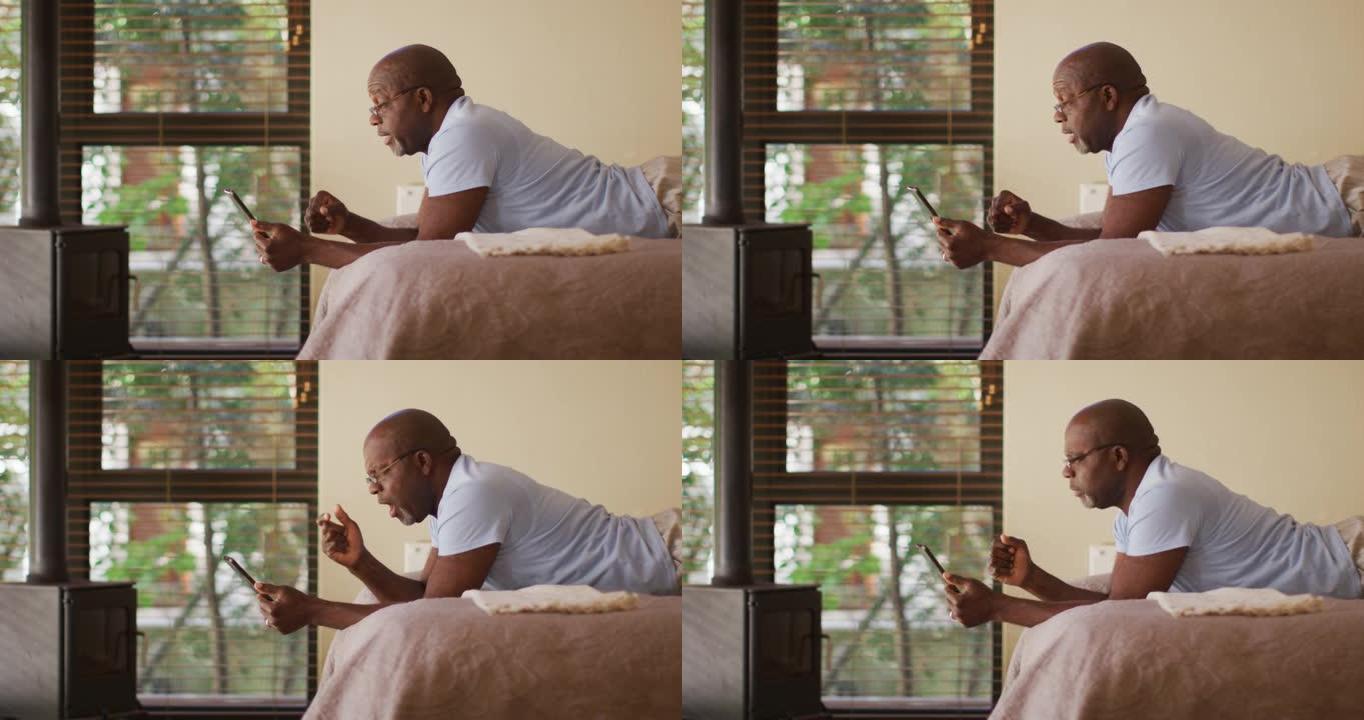 快乐的非洲裔美国老人躺在床上看平板电脑欢呼