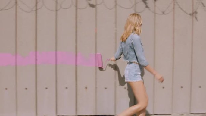 性感的女人画墙与粉红色的油漆走在城市街道自信的女艺术家享受城市涂鸦艺术4k的创造性表达