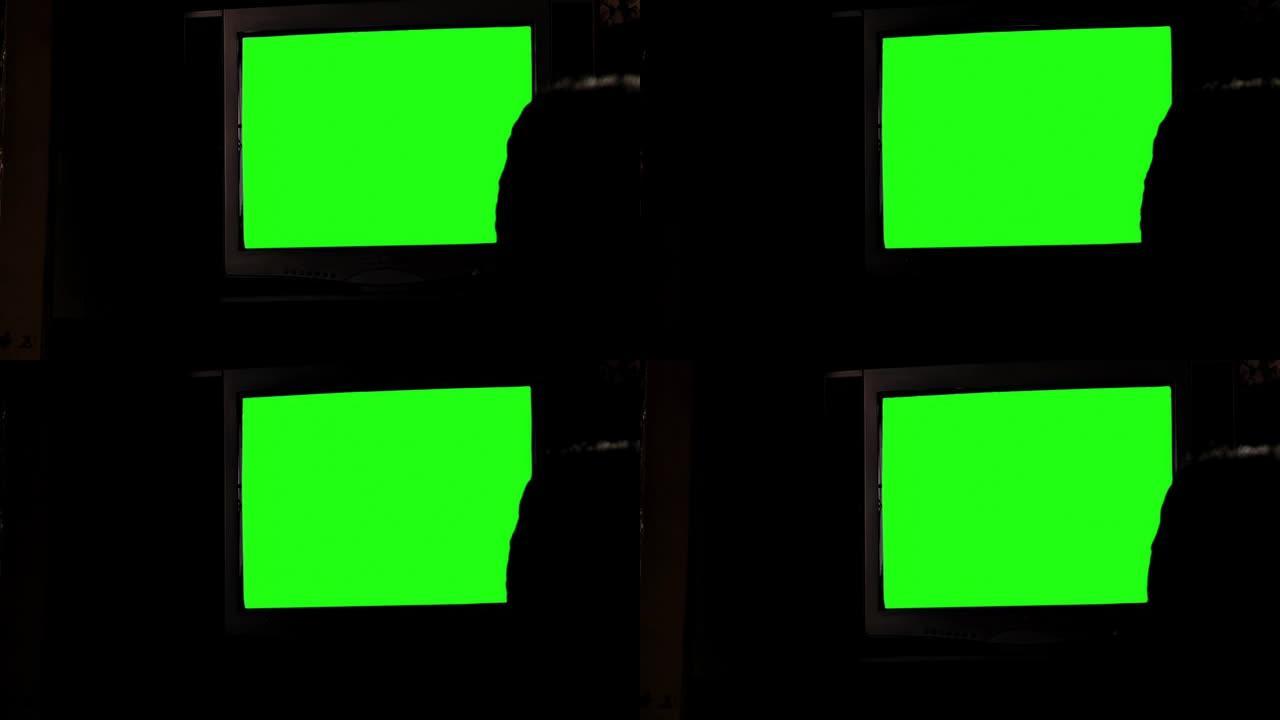 带有绿色屏幕的电视机和一个男人在黑暗房间里的轮廓。