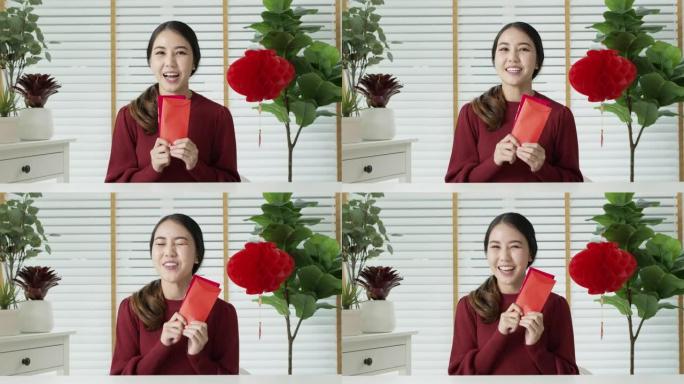 自拍视频拍摄红色中国新年庆祝装迷人的年轻亚洲女士快乐微笑交谈，看着手机拿着和展示红色零花钱或信封。