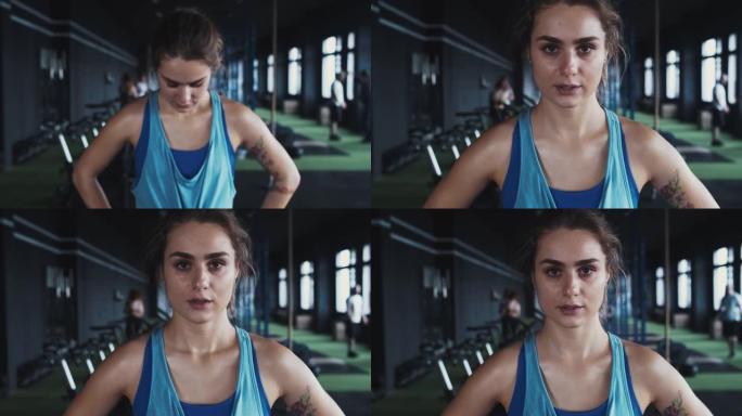 严肃美丽的年轻坚定女运动员的肖像看着相机，在当地健身房锻炼后汗流浃背。