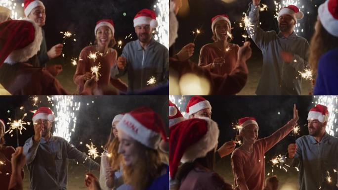 电影拍摄的是年轻的快乐微笑的多民族朋友，手里拿着圣诞老人的帽子和烟火，他们在晚上的户外庆祝晚会上唱歌