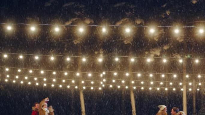 垂直视频。浪漫的冬夜: 滑冰夫妇在溜冰场上玩得开心。美丽的雪落在双人滑冰男孩和恋爱中的女友上，跳舞，