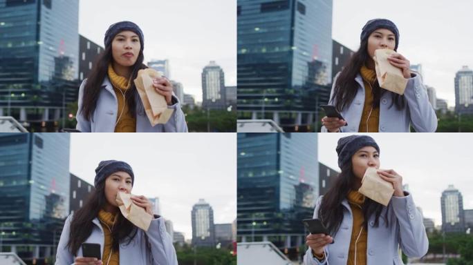 亚洲妇女使用智能手机走路并吃三明治