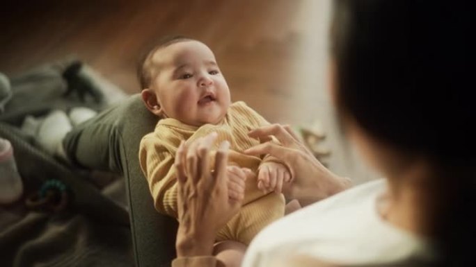 一个可爱的亚洲婴儿笑着，躺在他妈妈的腿上，一起享受亲密的时光，用爱看着她。顽皮的妈妈挠她的孩子和他玩