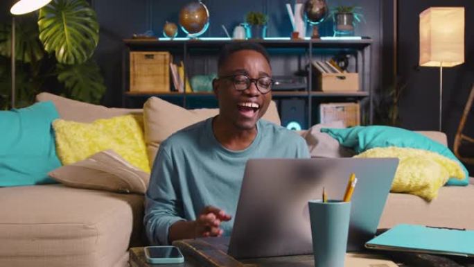 网络会议概念。快乐的年轻黑人男学生在客厅通过笔记本电脑网络摄像头视频通话与家人交谈。