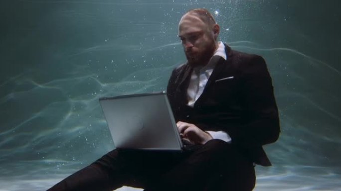 抽象过劳概念。年轻坚定的商人穿着办公服，使用笔记本电脑在水下慢动作下工作。
