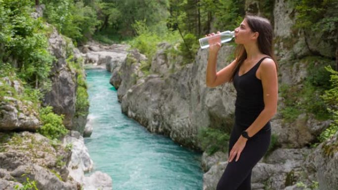 快乐的女游客在山溪享受壮丽的景色，喝水