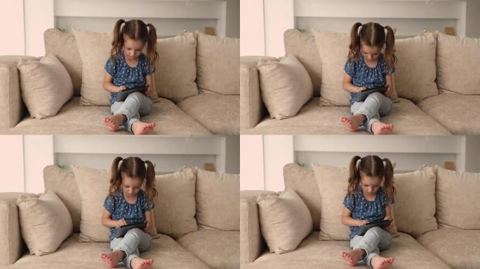 小严肃的女孩坐在沙发上玩电子游戏使用平板电脑