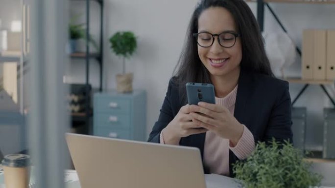 中东女性企业家使用智能手机发短信并在办公室室内微笑