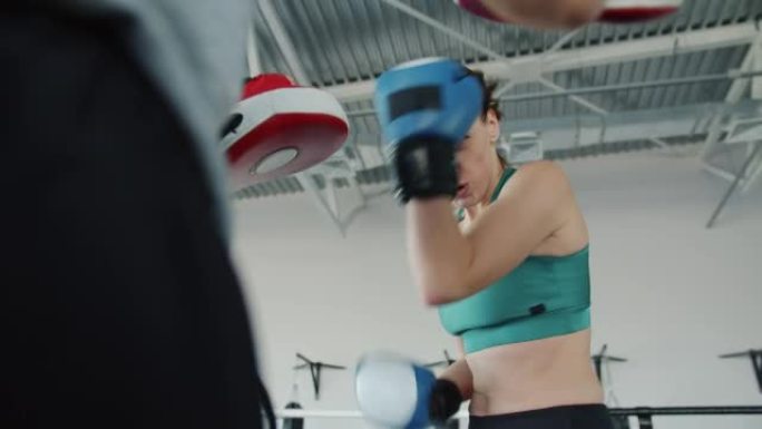 戴着拳击手套的职业女运动员在健身房与伴侣练习拳打