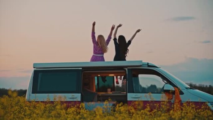 DS日落时，两个女人在乡下露营者的屋顶上挥舞着手臂，玩得很开心