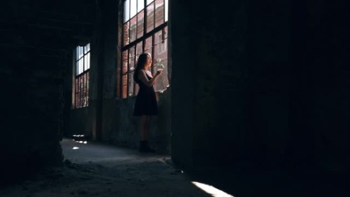 年轻女子独自在一座被毁的住宅楼中靠近窗户