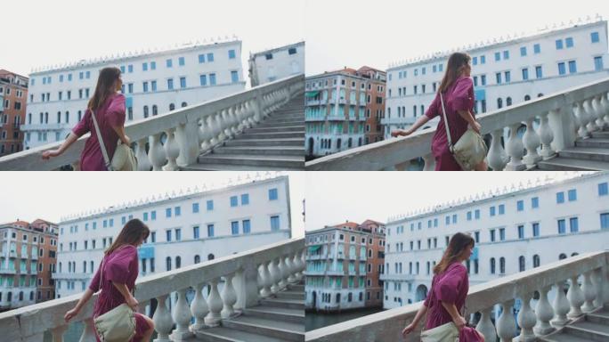 镜头跟随穿着紫色连衣裙的年轻快乐黑发白人旅游女人迅速走上威尼斯的老桥楼梯。