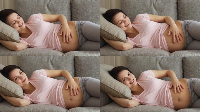 快乐孕妇躺在沙发上抚摸她的大肚子
