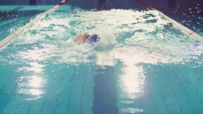 成功的男子游泳运动员赛车，在游泳池游泳。职业运动员决心使用自由泳赢得冠军。彩色电影镜头。后视图跟踪慢