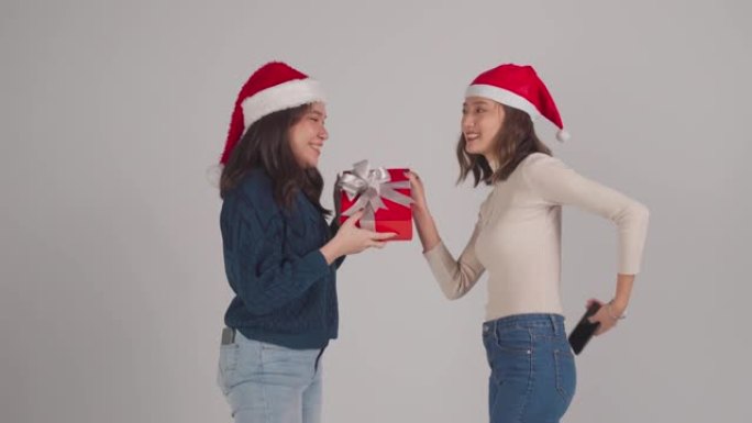 亚洲华裔女性朋友玩得开心自拍和圣诞派对礼物交换工作室拍摄灰色背景